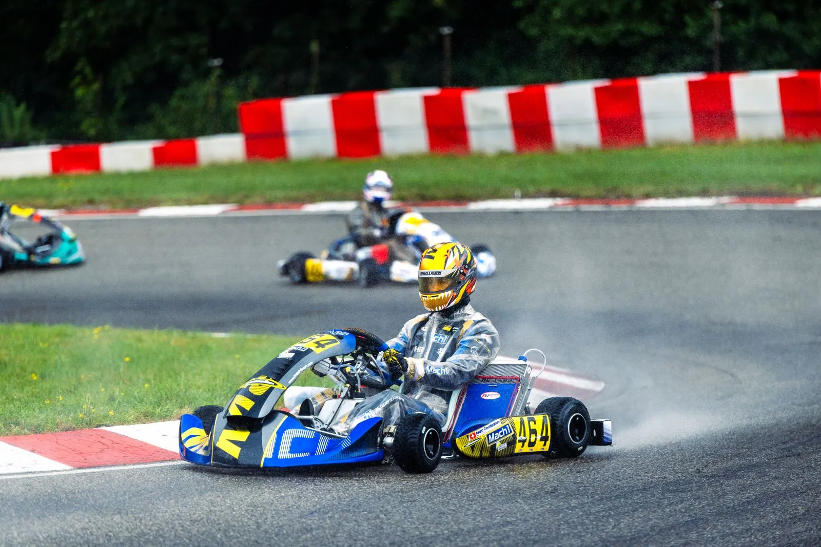Mach1 Rennkart mit Fahrer im gelben Helm in der Kurve, im Hintergrund ein weiteres Kart